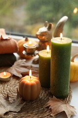 Burning candles and dry leaves on windowsill on rainy day. Autumn atmosphere
