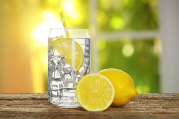 Lemon water and ice cubes in glass on wooden table against window indoors
