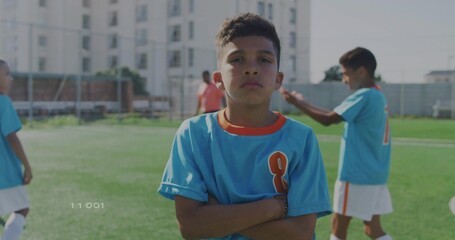 Standing soccer player in blue orange uniform crossing arms on turf field, with coach observing