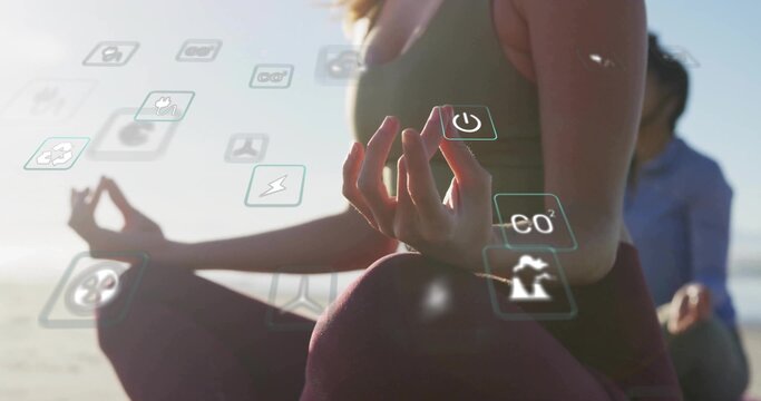 Practicing woman wearing activewear meditating on sandy shore at sunrise, with floating eco icons