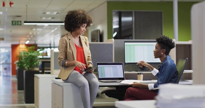 Discussing two colleagues in business casual sharing data on tablet and laptops in open-plan office - Powered by Adobe