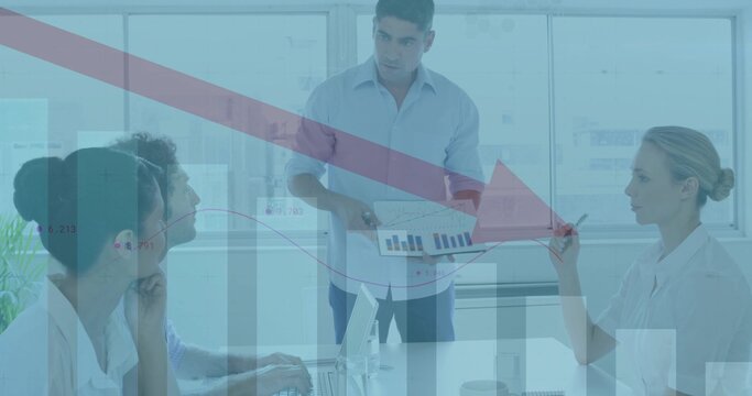 Pointing male presenter wearing suit showing printed chart in conference room, with laptops pens