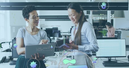 Reviewing code two women collaborating at desk in open-plan tech office, with laptop and tablet