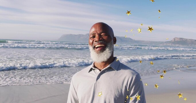 Smiling senior man standing on sandy shoreline by ocean waves, with floating golden star overlays - Powered by Adobe