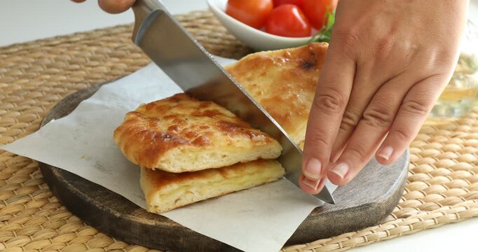 Woman cutting delicious Megrelian khachapuri at table, closeup