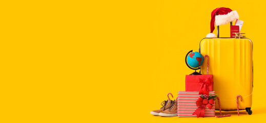 Suitcase with winter and travel accessories on yellow background