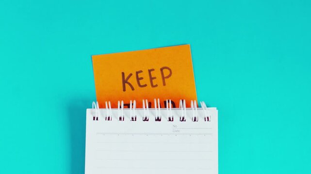 Sticky notes with the words 'KEEP IT UP!' hidden behind office supplies isolated on blue background