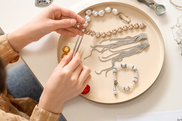 Young female jewelry designer making bracelet on table, top view