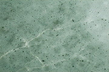 Textured abstract background in dusty teal or muted green with countless black specks, featuring a distinct, jagged white crack or vein running across the surface like fractured ice or weathered stone