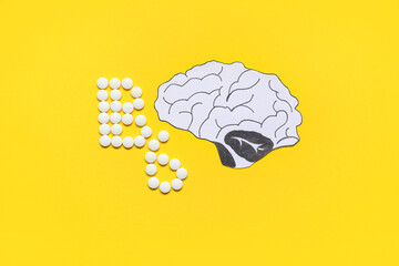 Vitamin B6 pills with paper brain on yellow background