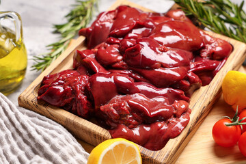 Wooden board with raw liver, rosemary, cut lemon and tomatoes, closeup