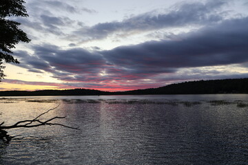 A panoramic view of a lake in the Adirondacks during a beautiful sunset illuminating the sky with red and gold.