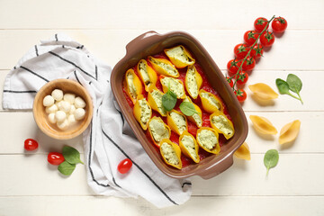 Baking dish of stuffed conchiglie pasta with cheese, spinach and tomato sauce on white wooden background