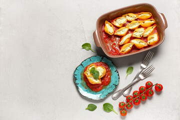 Baking dish and plate of stuffed conchiglie pasta with cheese, spinach, tomato sauce on grey background