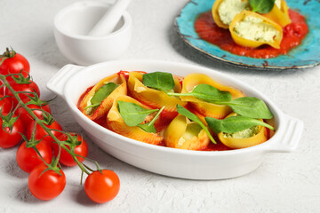 Baking dish of stuffed conchiglie pasta with cheese, spinach and tomato sauce on light background
