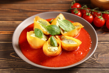 Plate of stuffed conchiglie pasta with cheese, tomato sauce and spinach on wooden background