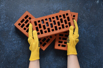 Hands of builder in gloves with bricks on blue grunge background