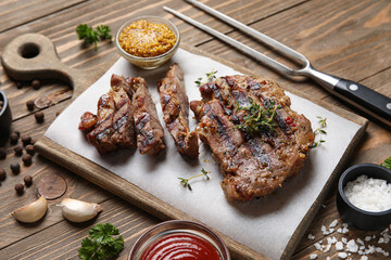 Tasty grilled steaks with mustard and fork on wooden background