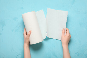 Woman tearing paper towel from roll on blue background