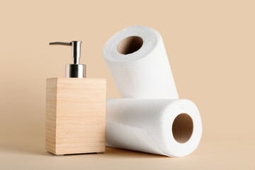 Bottle with soap and rolls of paper towels on beige background