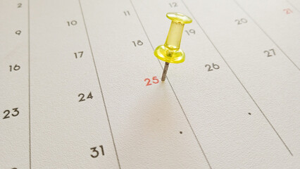 Close-up of a thumbtack pinning the 25th on a calendar to signify a special event or schedule....