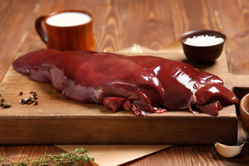 Raw liver with jug of milk, thyme, peppercorns and sea salt on wooden background
