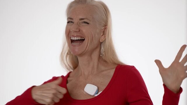 Happy excited mature woman expresses joy while wearing a heart monitoring device for atrial fibrillation. She promotes health awareness and proactive healthcare.