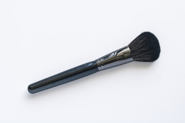 A professional makeup brush with soft black bristles and a sleek, dark handle, placed diagonally on a plain white background.