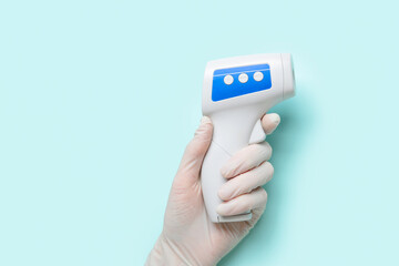 Hand of doctor in rubber glove with infrared thermometer on turquoise background