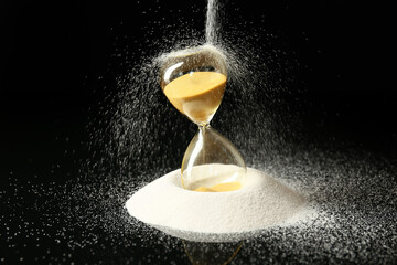 Crystal hourglass and pouring sand on dark background