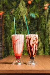 Two milkshakes of different flavors on a wooden table.