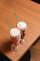Top view of two milkshakes on a wooden table.