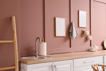 Interior of stylish kitchen with white counters, ladder and utensils near brown wall