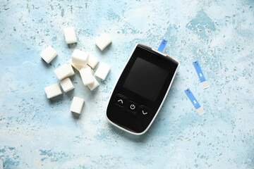 Glucometer with test strips and sugar cubes on blue grunge background