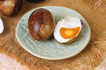 Asian grilled salted egg cut in half with orange yolk, presented on rustic ceramic plate.