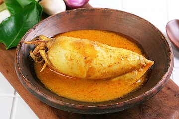 Close-up of gulai cumi, Indonesian squid curry with coconut milk, served in wooden bowl with spices.