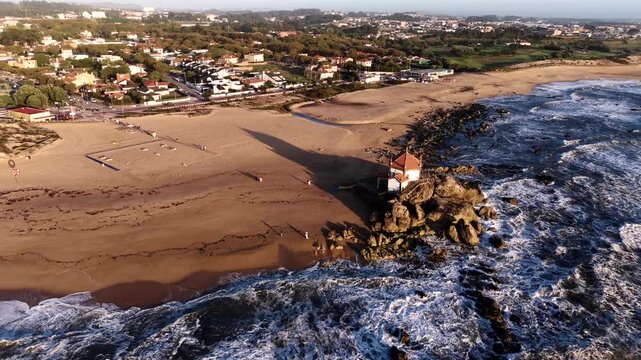 Capela do Senhor da Pedra chapel surrounded by waves and golden sand on Miramar beach Portugal