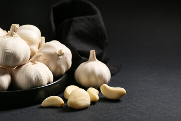Plate with fresh garlics on black background
