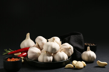 Plate with fresh garlics and different spices on black background