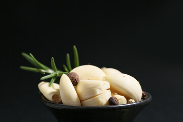 Bowl with fresh garlic cloves, peppercorns and rosemary on black background, closeup