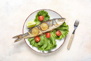 Plate with delicious cooked seabass fish, lettuce, tomatoes and lemon slices on light background