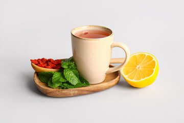 Cup of hot goji tea with mint and lemon on grey background