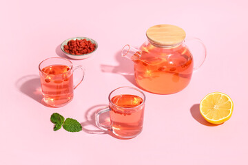 Glass cups of hot goji tea with mint and lemon on pink background