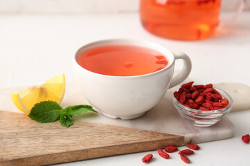 Cup of hot goji tea with lemon and mint on white background, closeup
