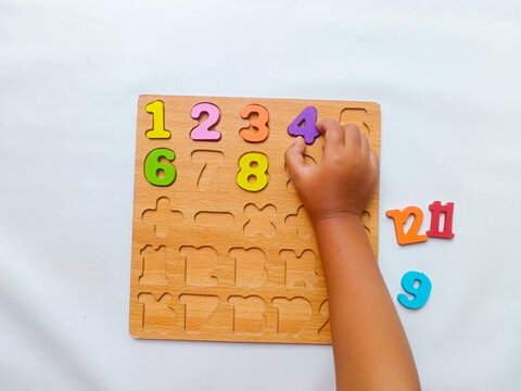 Child’s hand playing with colorful wooden number puzzle on a white background. Education toy. Learning through play concept