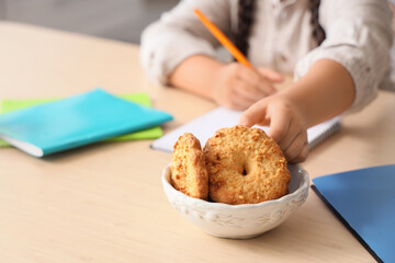 Little girl with tasty cookies doing homework at table in kitchen, closeup