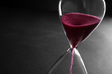 Hourglass with pink crystals on black background, closeup. Time management concept