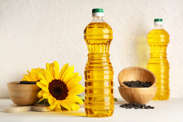 Bottles of oil, sunflowers and bowls with seeds on light background