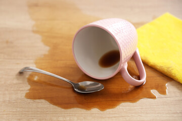 Overturned cup with spoon and spilled coffee on table in kitchen, closeup