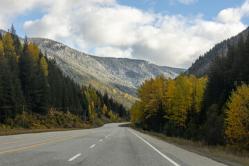 A highway drives through the Cascade Mountains with yellow autumn leaves and fresh snowfall near Manning Park, British Columbia, Canada